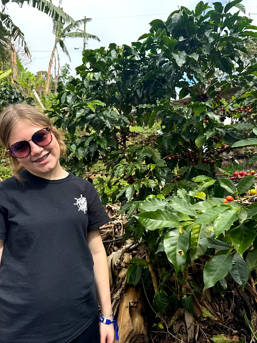 A young visitor smiling beside the coffee trees on the farm