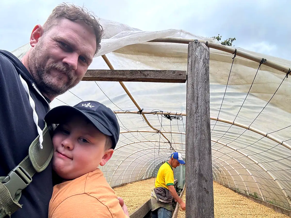 A father and his son together in the drying house at the farm, a worker turning coffee behind them