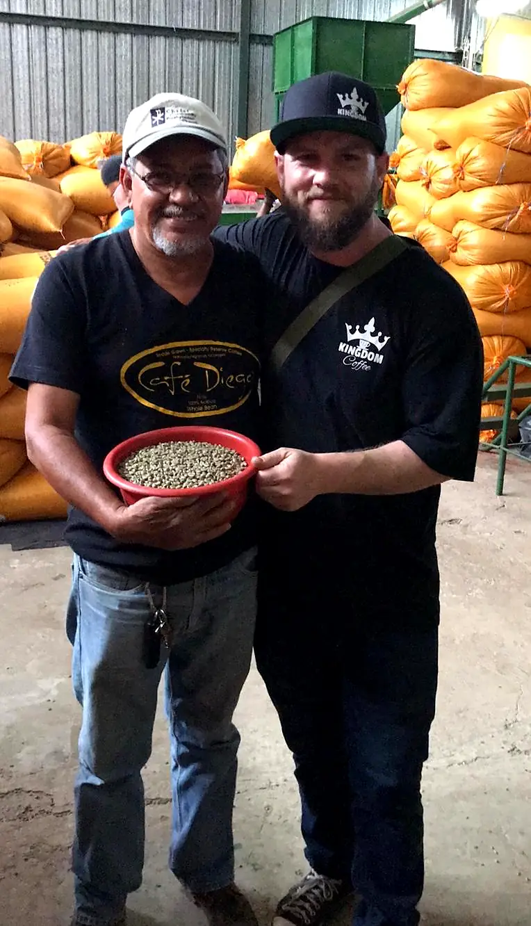 Our buyer standing arm in arm with a coffee producer at the mill, holding a bowl of green coffee beans