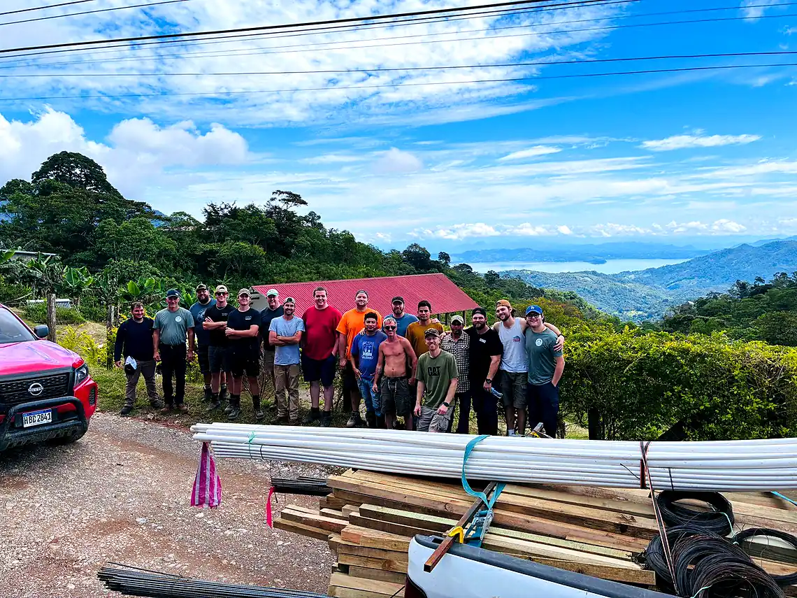 The whole team standing together on a hillside at the farm, valley and mountains behind them