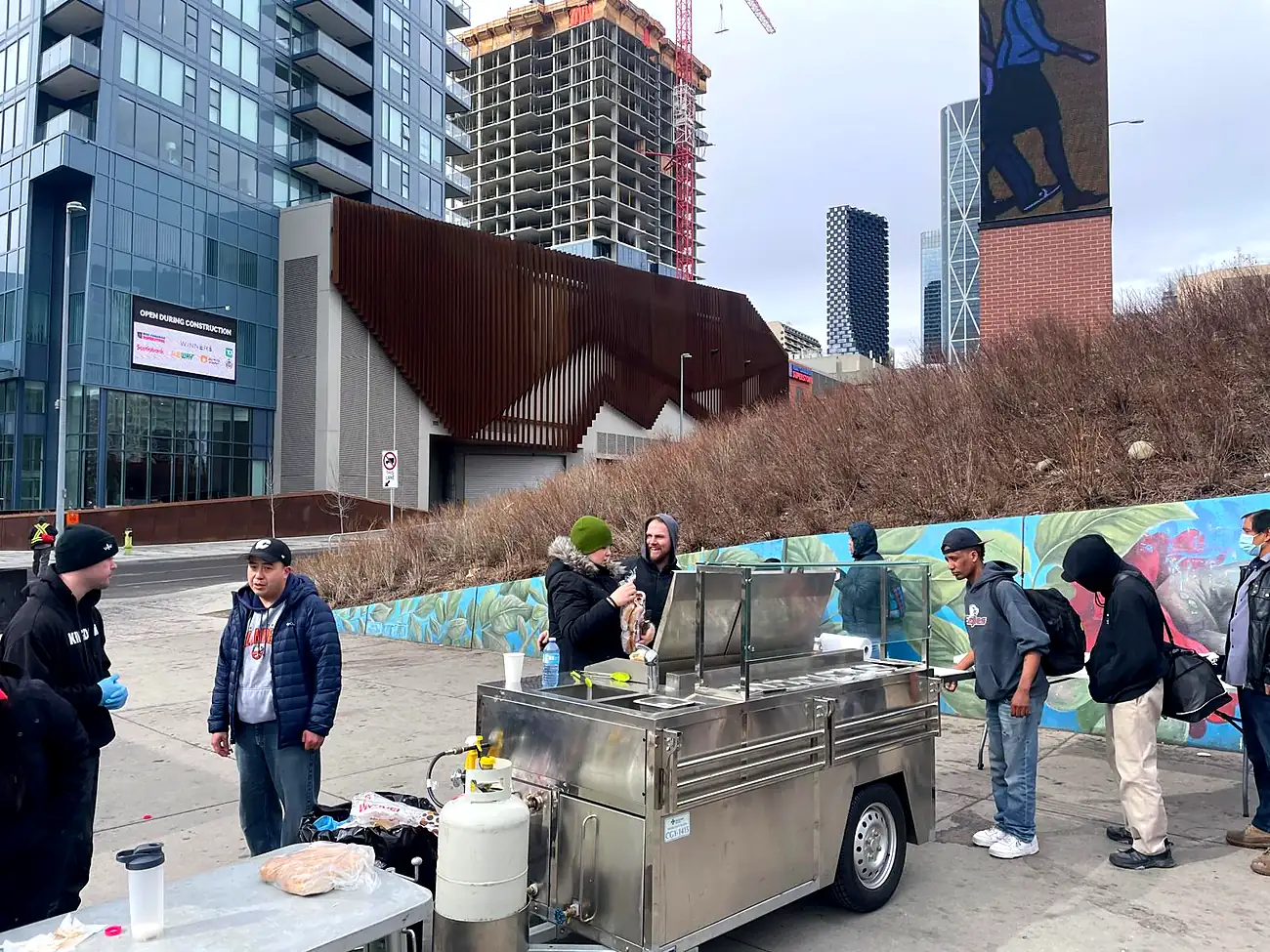 A hot meal and coffee cart set up on the sidewalk with people being served