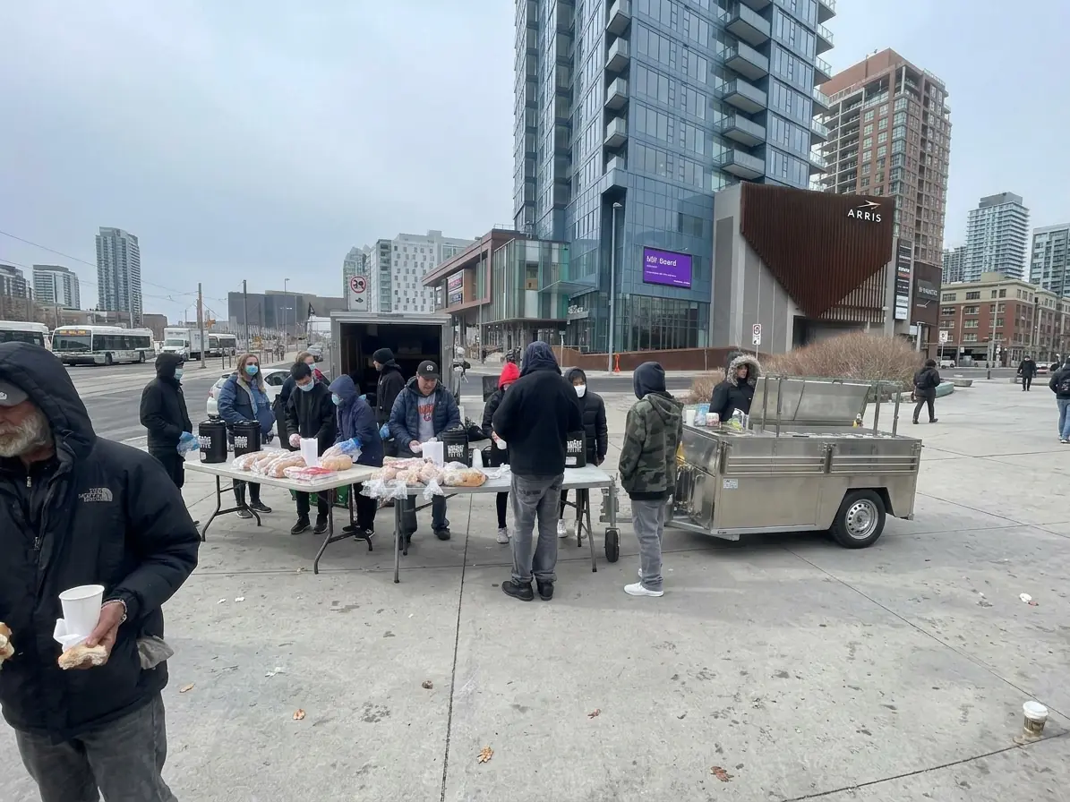 Volunteers handing out hot meals and coffee from a street cart on a downtown sidewalk